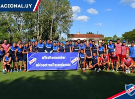 El plantel completo de Nacional en Primera División y el Equipo Técnico, con la pancarta que dice We Remember y Nosotros Recordamos, de fondo azul, con el escudo de Nacional a ambos costados. Letras blancas.