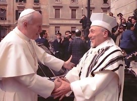 El Papa, de blanco y el rabino, cubierto con el Talit, extendiendo mutuamente los brazos sonriendo ambos y tomándose las manos