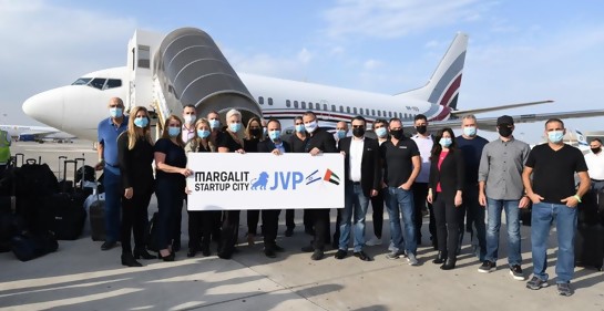 Un grupo de empresarios junto a un avión, con un cartel que dice Margalit Start up city