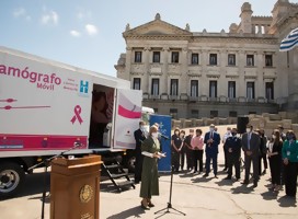 Un grupo de gente, con el parlamento uruguayo de fondo, junto a un vehículo en el que dice mamógrafo móvil